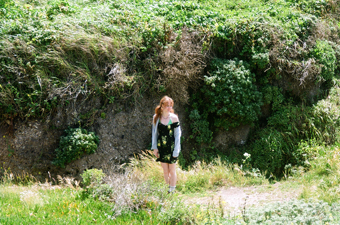 Photo of Grace Cookston, a girl with red hair, wearing a black dress and standing in an area surrounded by plants.